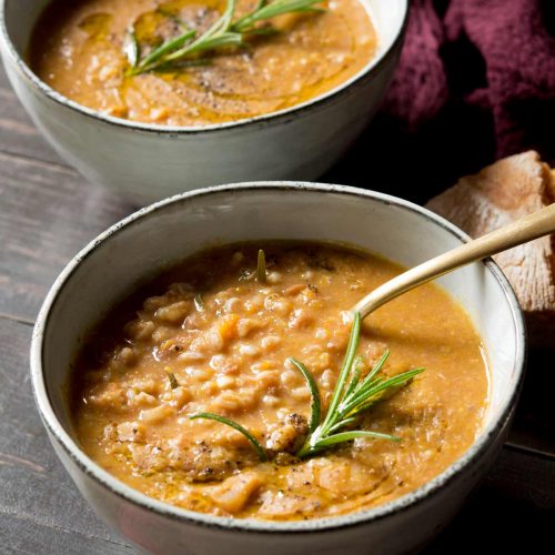 Tuscan farro soup in a bowl with a spoon and rosemary