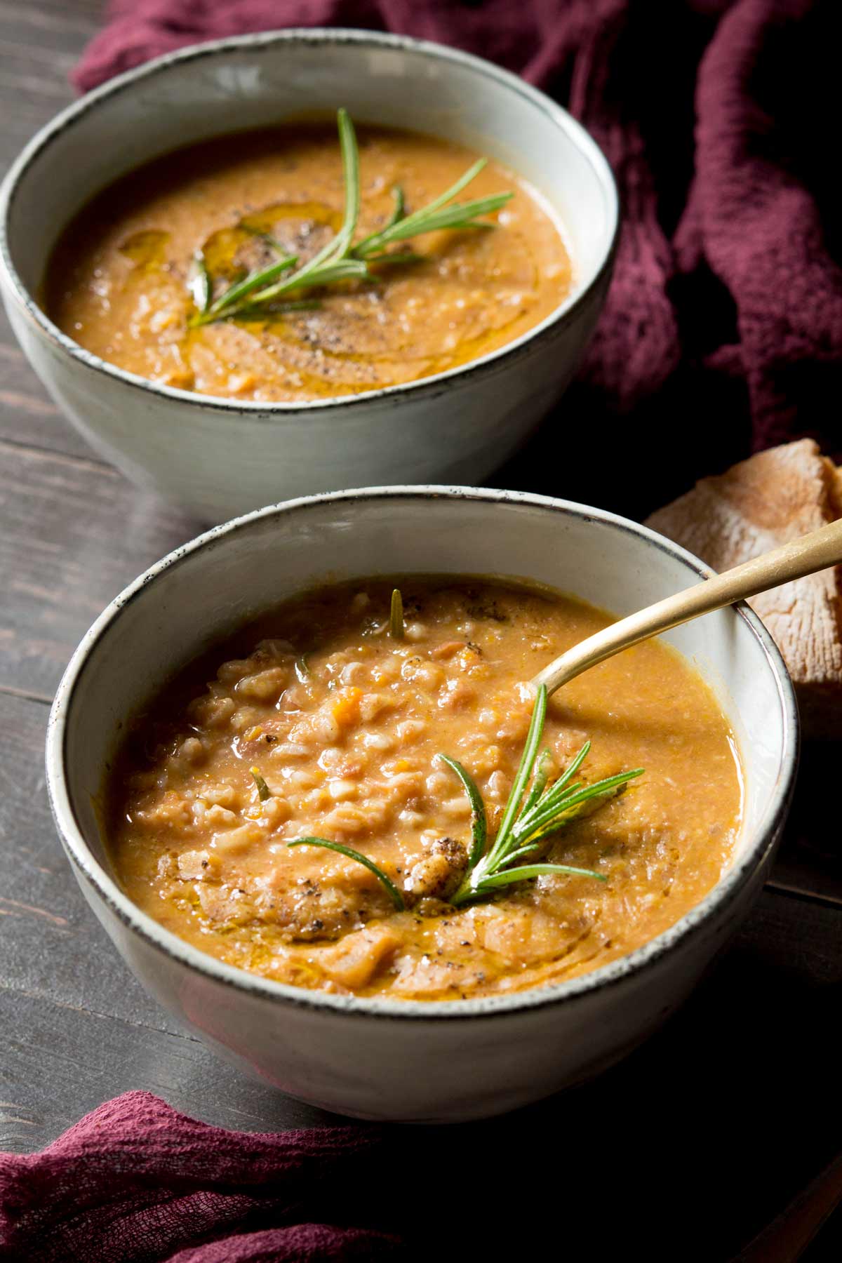 Tuscan farro soup in a bowl with a spoon and rosemary