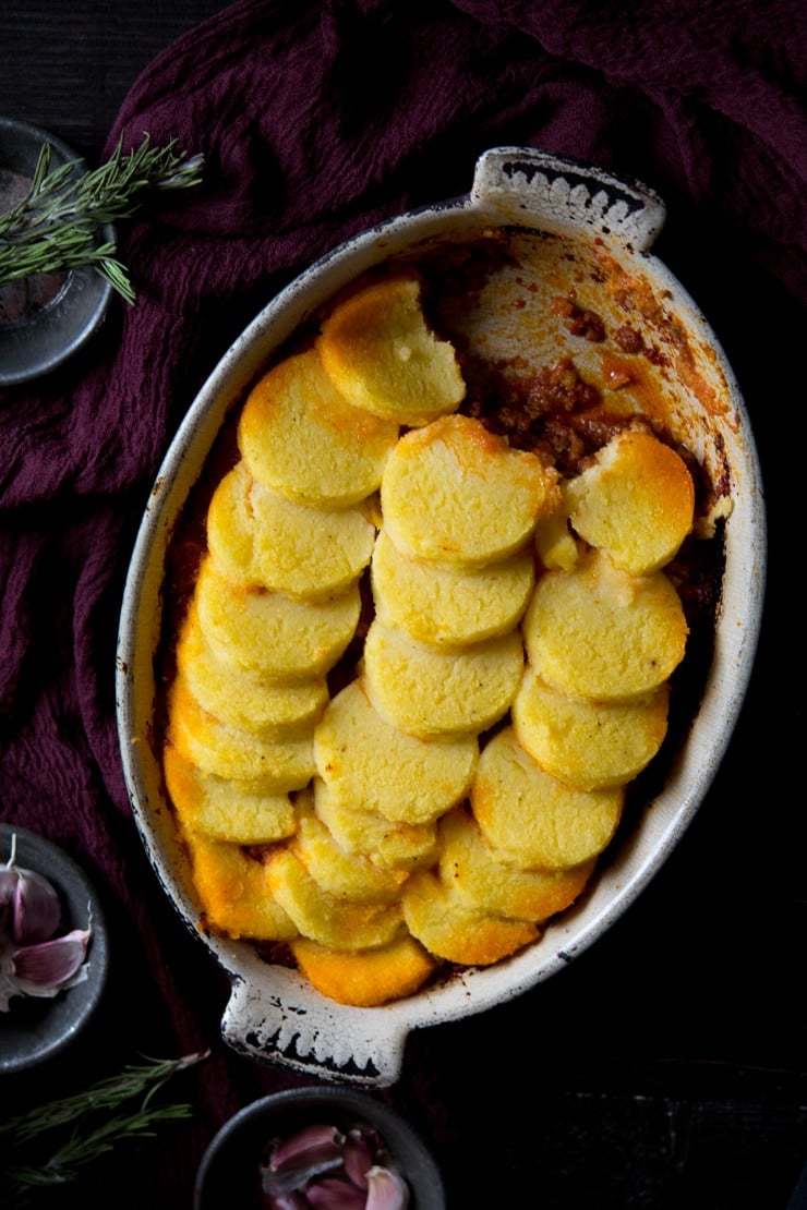 Beef and sausage ragu with baked polenta on top in an oval baking dish