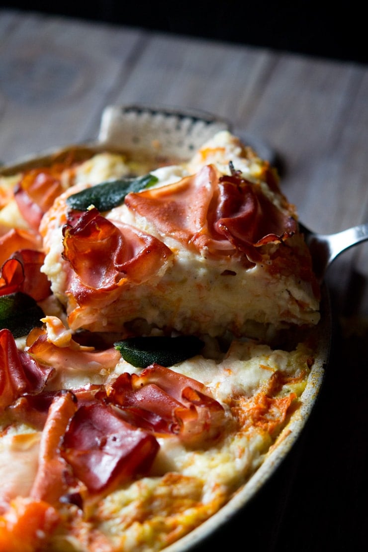 A close up shot of a slice of butternut squash lasagna topped with prosciutto