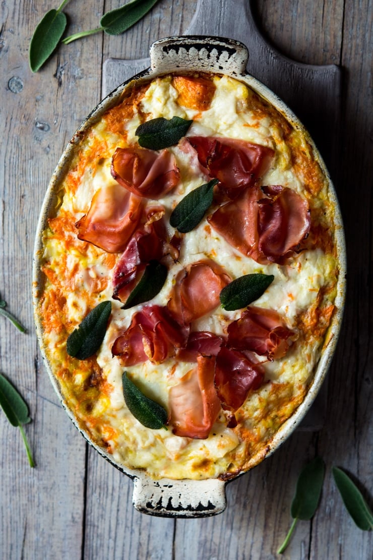 An overhead shot of butternut squash lasagna in an oval baking dish topped with prosciutto and sage leaves