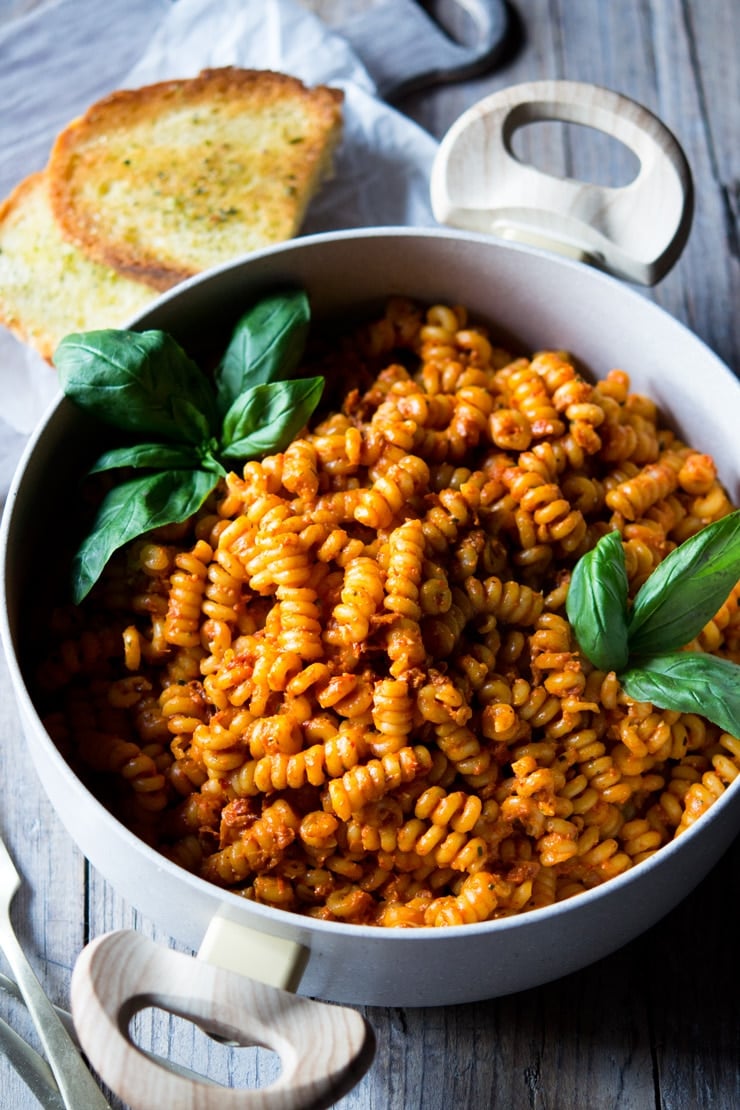 sun dried tomato pasta in a pot with basil and garlic bread