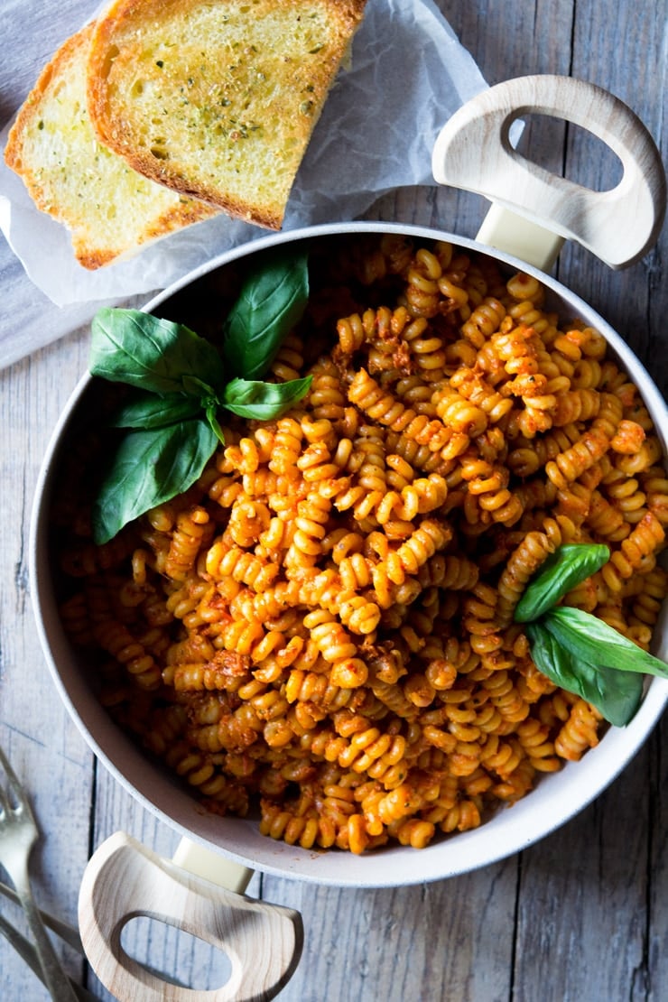 An overhead shot of sun dried tomato pasta in a large pot with basil