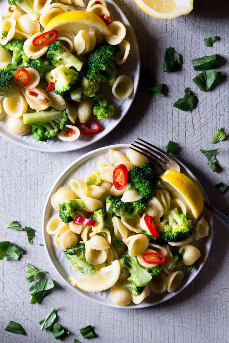 An overhead shot of two plates of broccoli pasta with scattered basil leaves