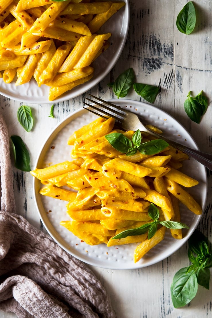 An overhead shot of butternut squash pasta on a plate with basil and a fork at the side