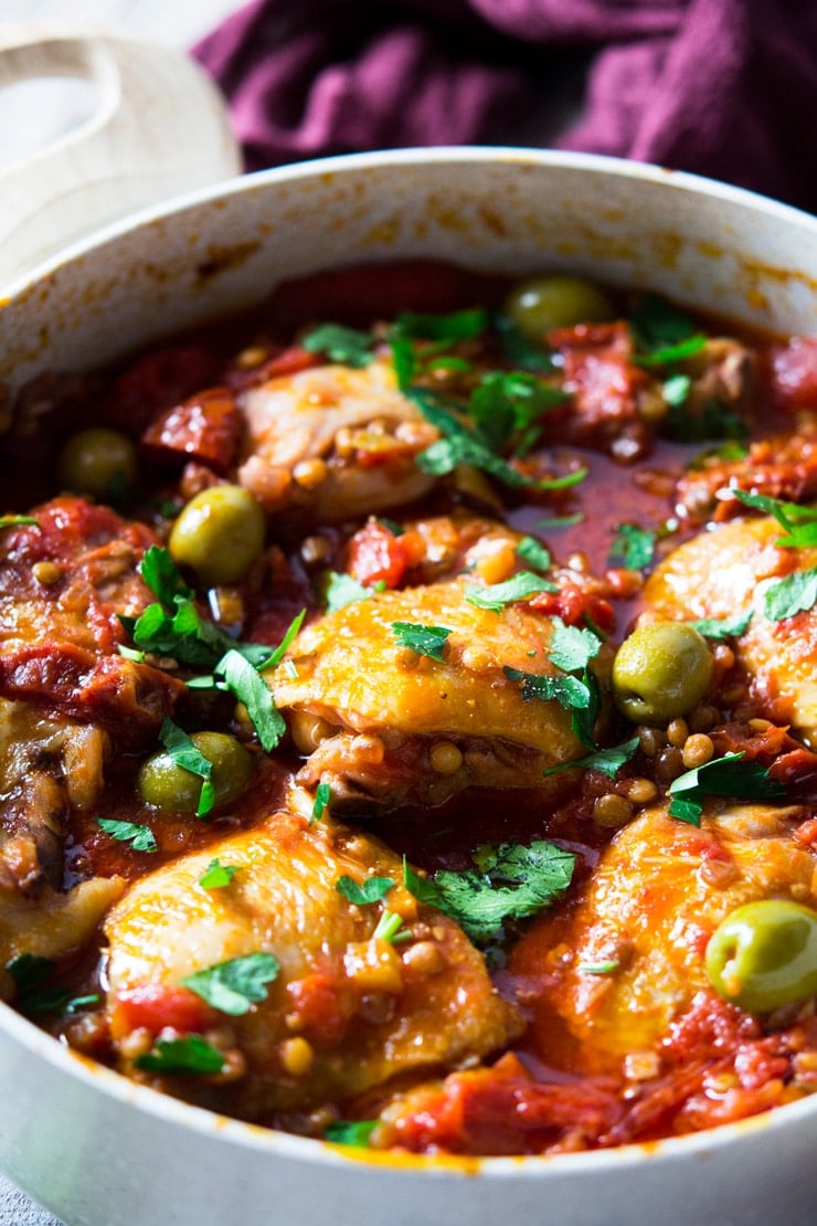 A close up of braised chicken with olives, tomatoes and lentils in a large pot