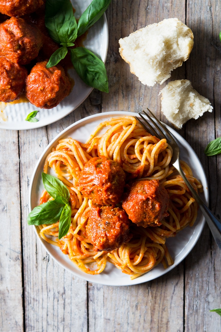 An overhead shot of mozzarella stuffed meatballs and spaghetti on a wooden surface with torn bread