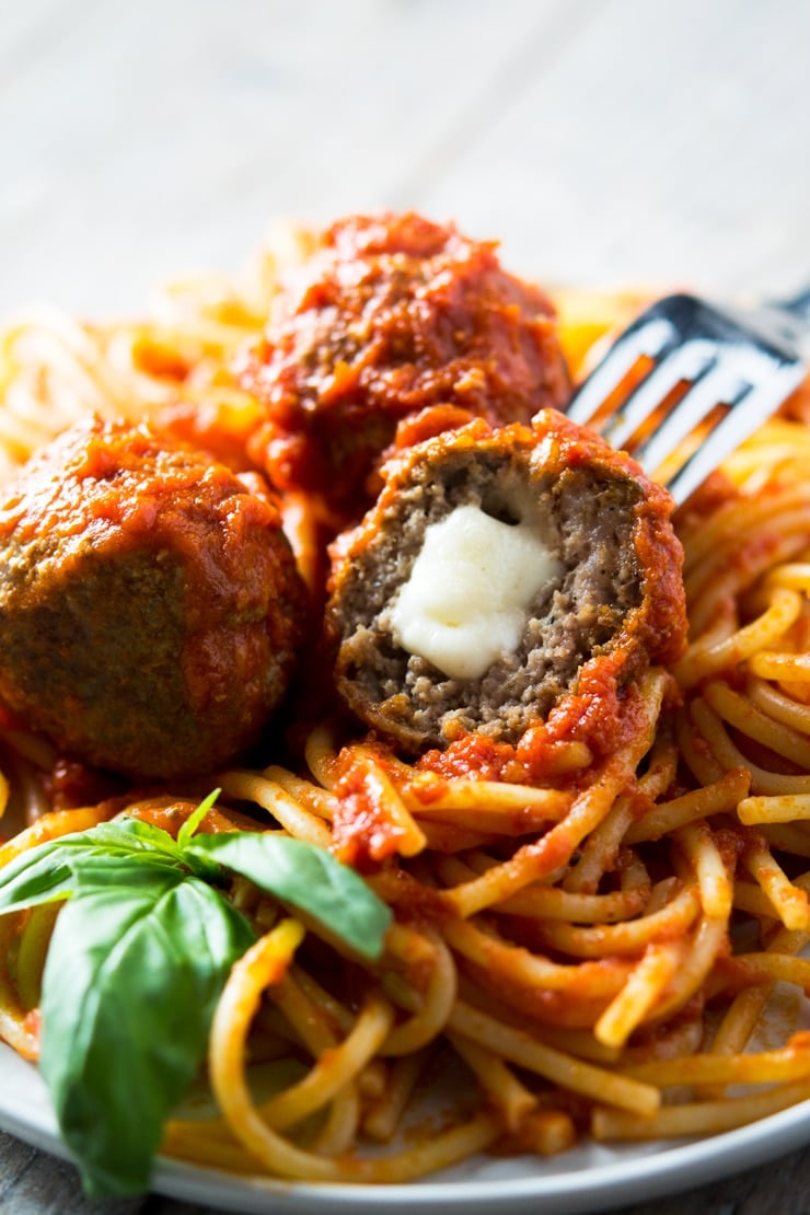 a close up of a mozzarella stuffed meatball on a fork in a plate of spaghetti