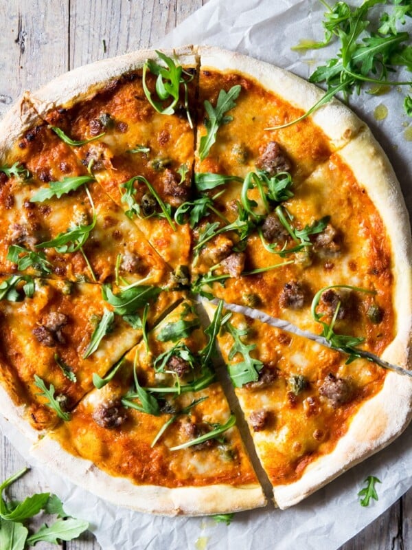 pizza with sausage and mozzarella, arugula and red pepper sauce on a wooden surface