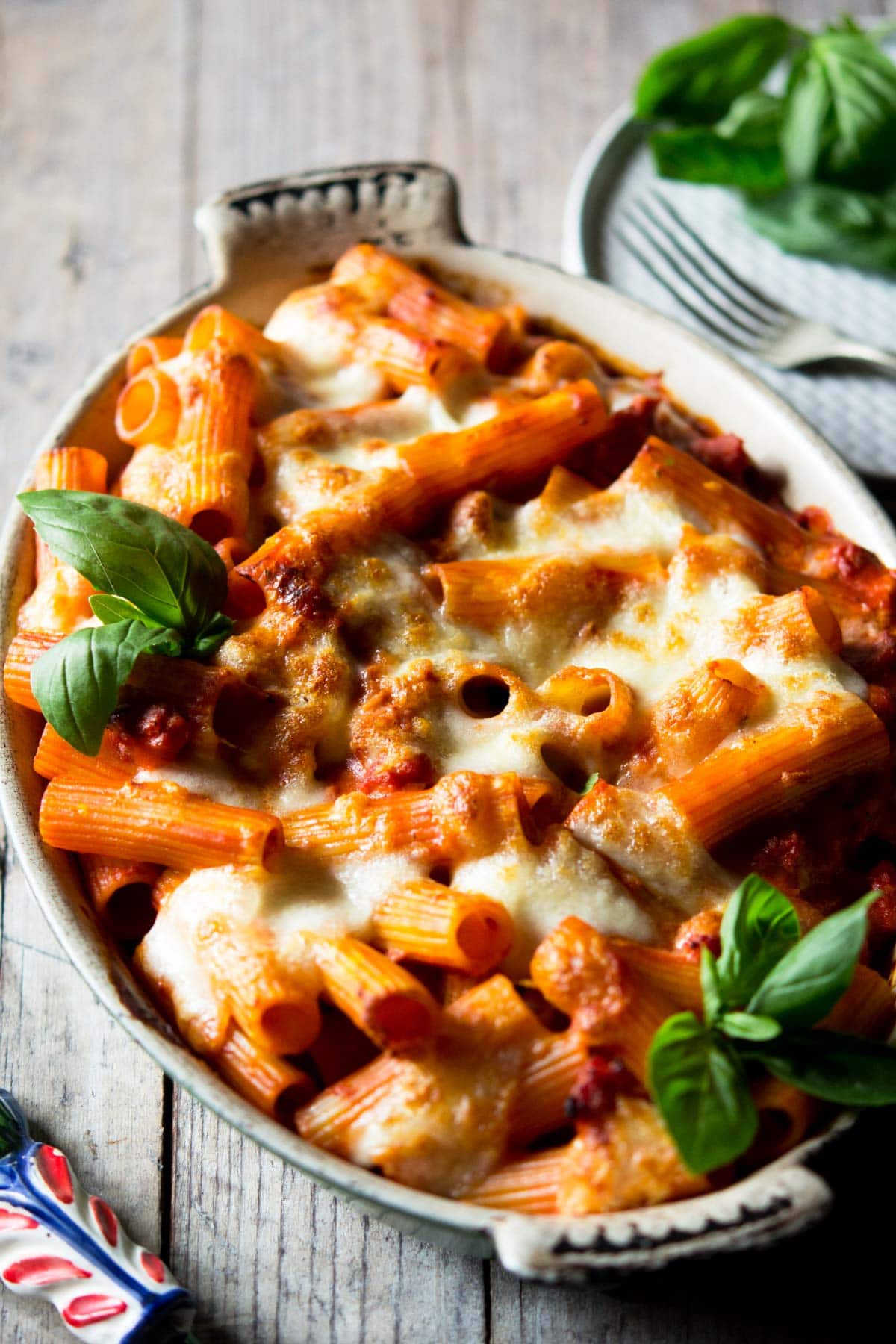 A close up of sausage pasta bake in a casserole dish topped with basil