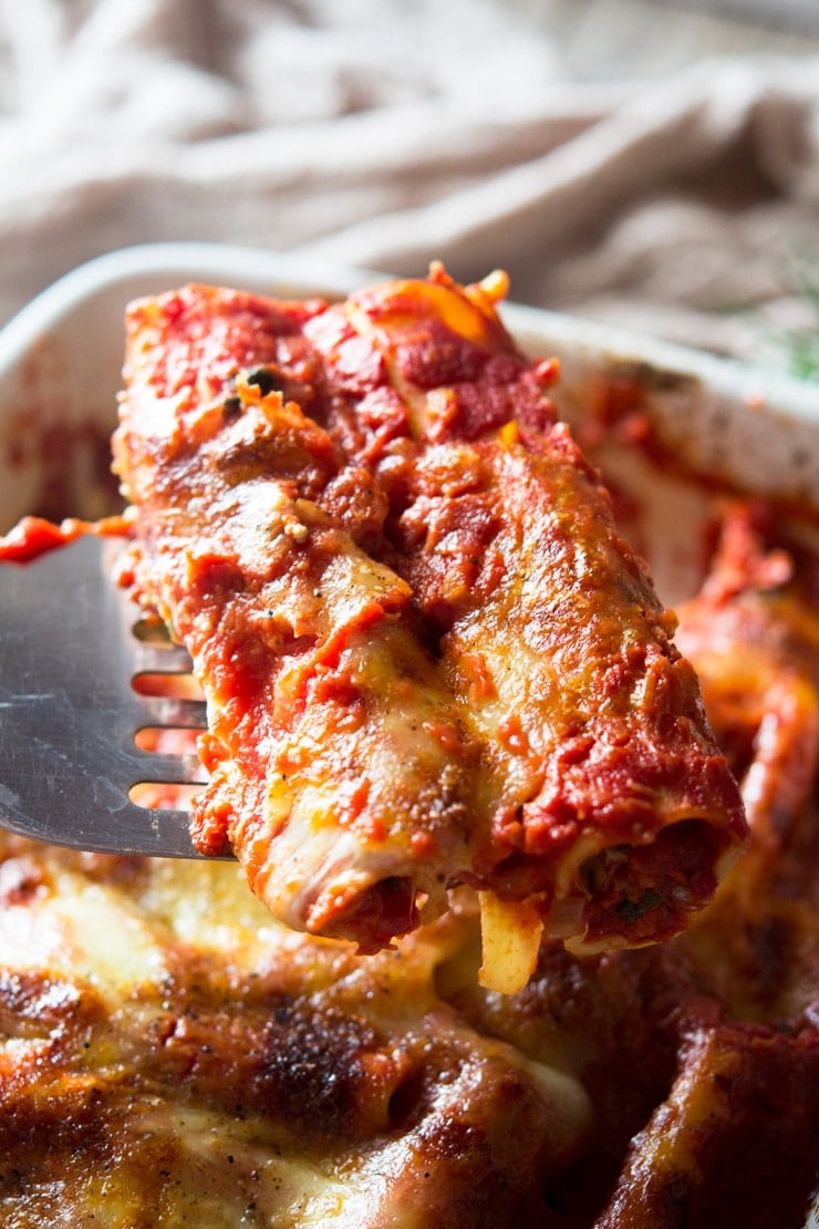 a close up of two spianch and ricotta cannelloni tubes on a serving spoon