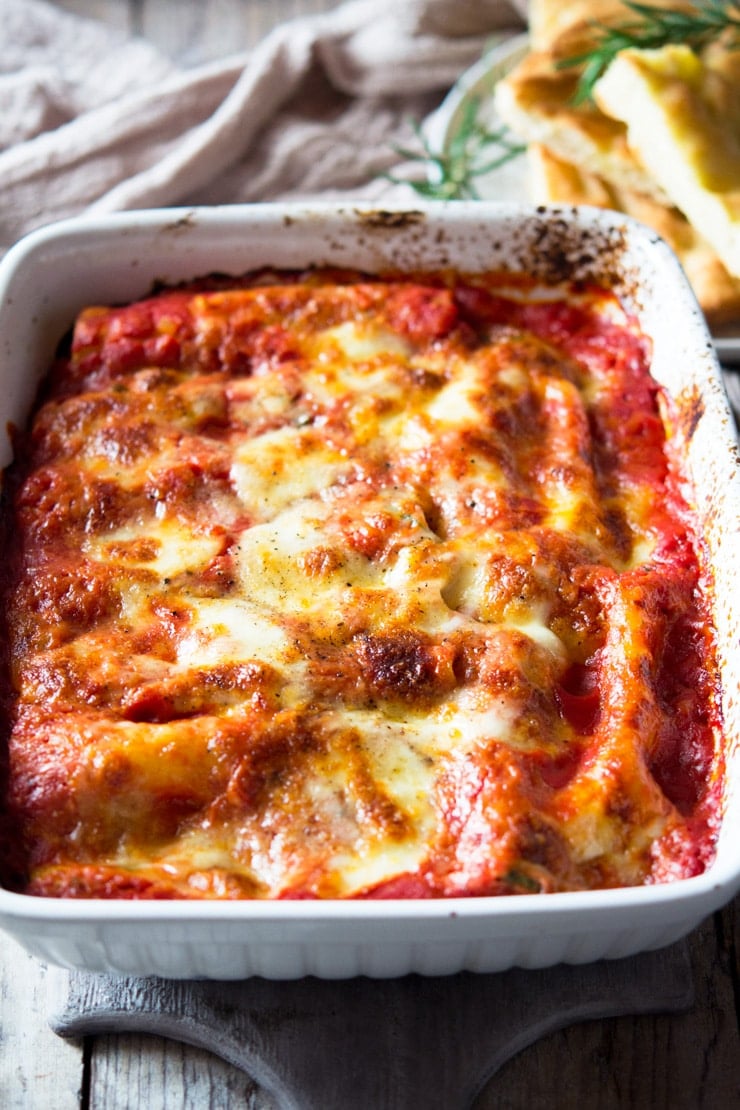 A close up of spinach and ricotta cannelloni in a large baking tray topped with melted mozzarella cheese