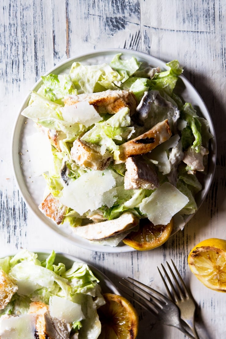 an overhead shot of a grilled chicken caesar salad on a wooden surface