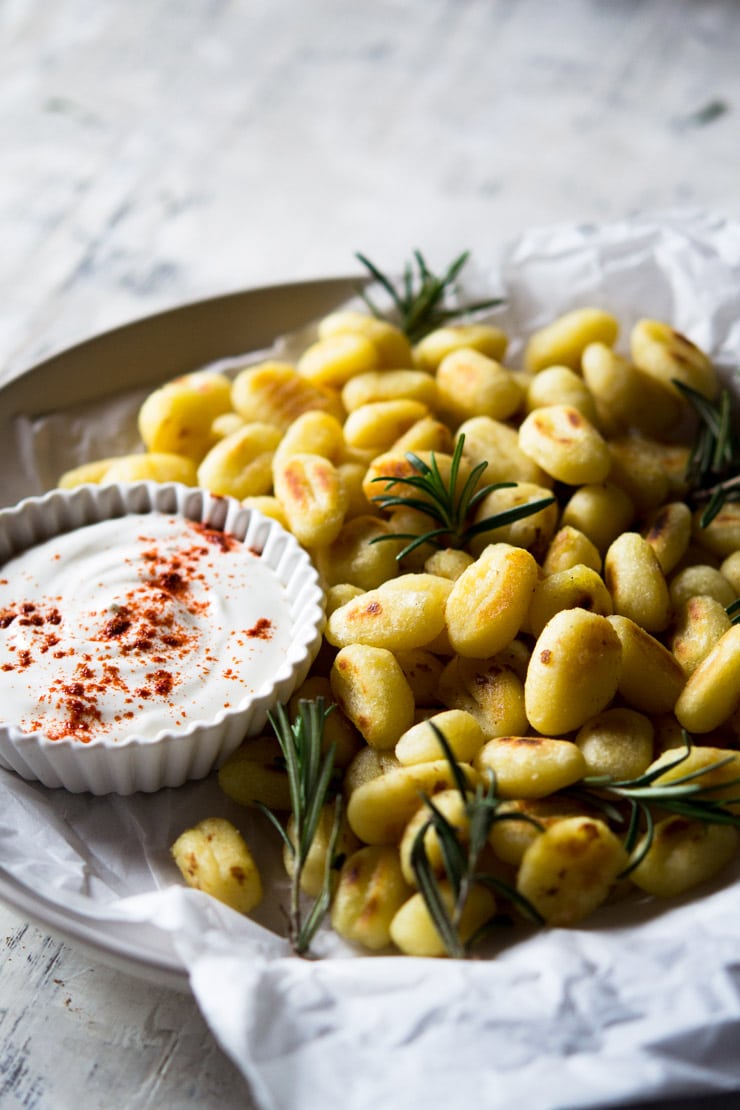 A close up of fried gnocchi on a plate with rosemary and a sour cream dip