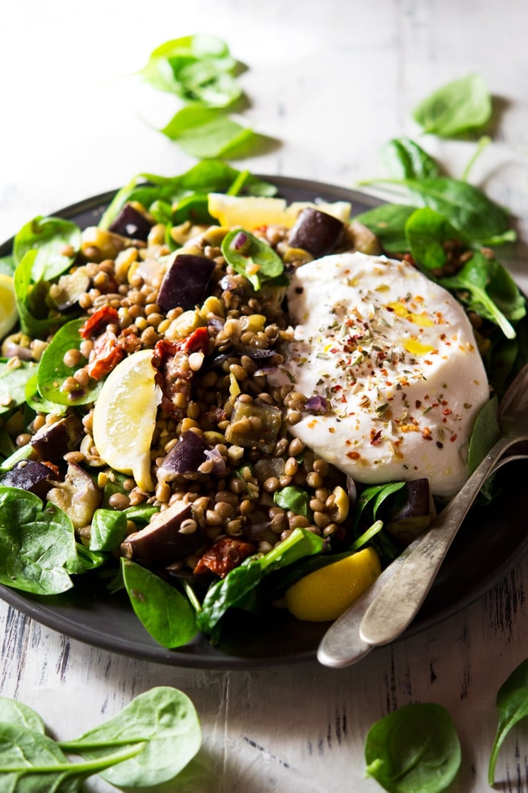 A close up of lentil salad with eggplant and burrata on a plate topped with herbs and spices