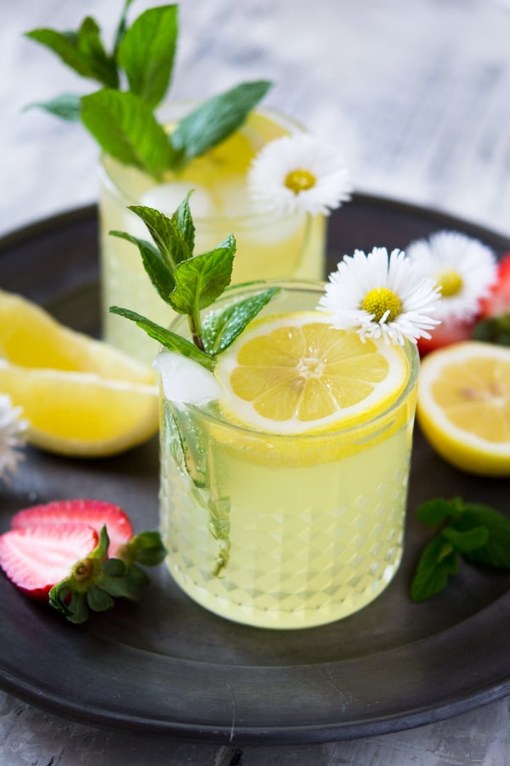 A close up of a limoncello cocktail on a pewter plate with mint and flowers