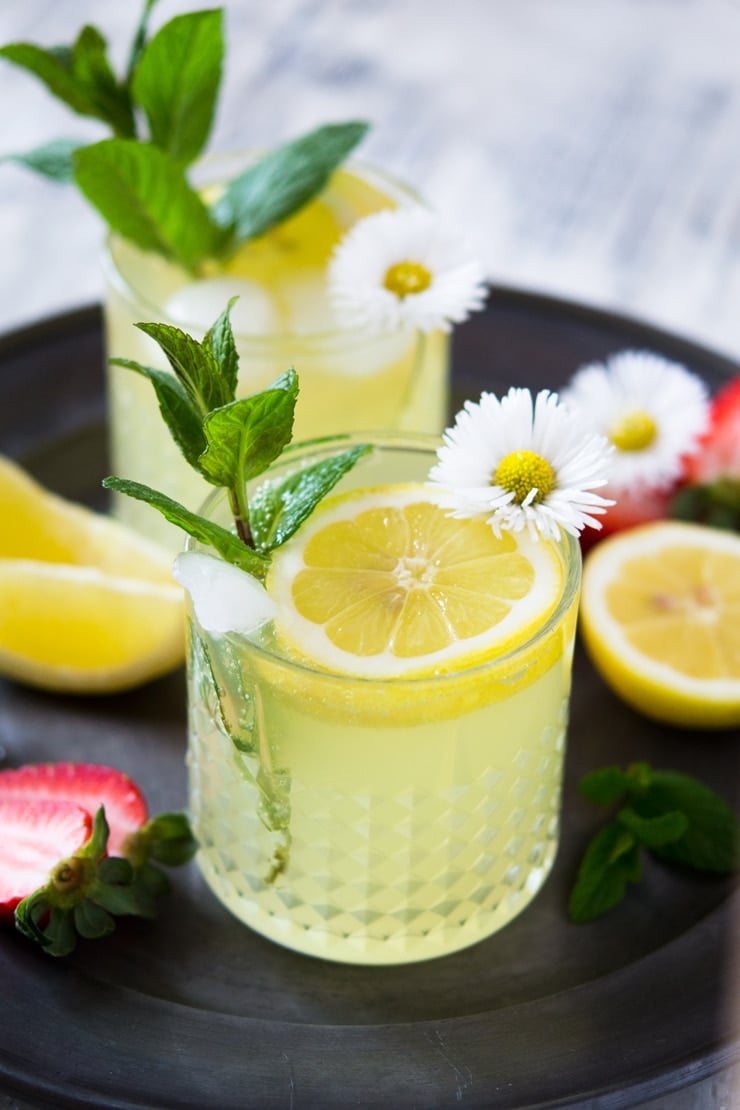 A photo of a limoncello cocktail on a pewter plate garnished with mint leaves and daisies