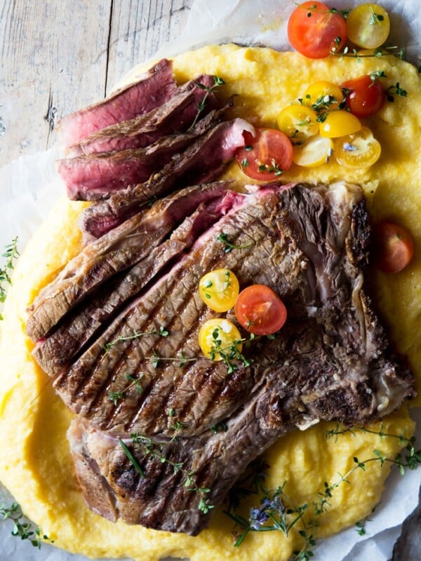 A florentine steak on a bed of polenta with some herbs
