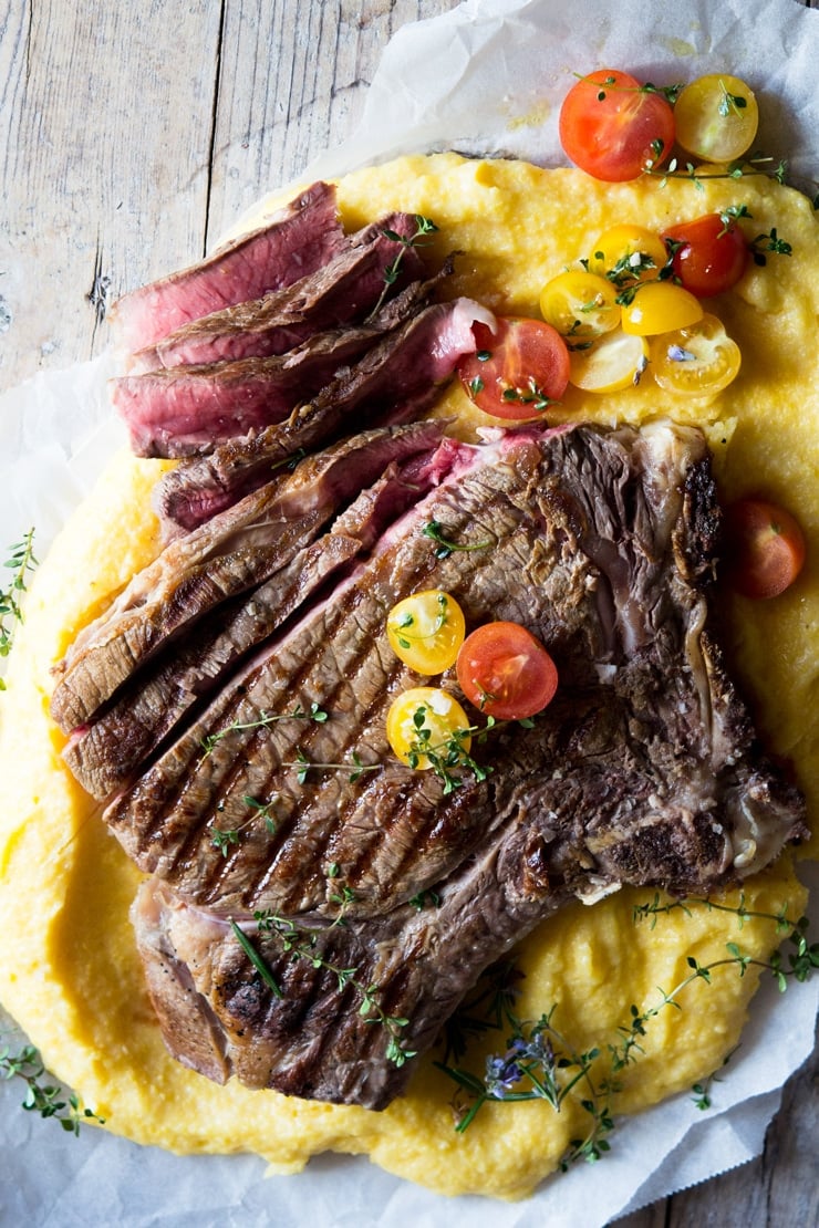 An overhead shot of a Florentine steak on a wooden surface with herbs