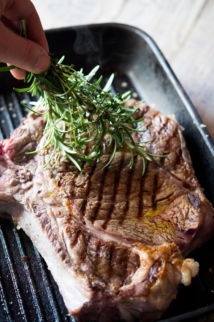 A hand brushing herbs over a Florentine steak