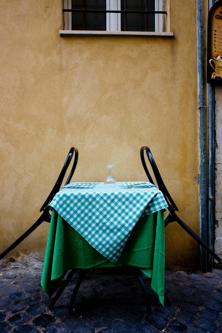 A photo of a yellow outside wall of a building with a table with a green checkered tablecloth and two back seats