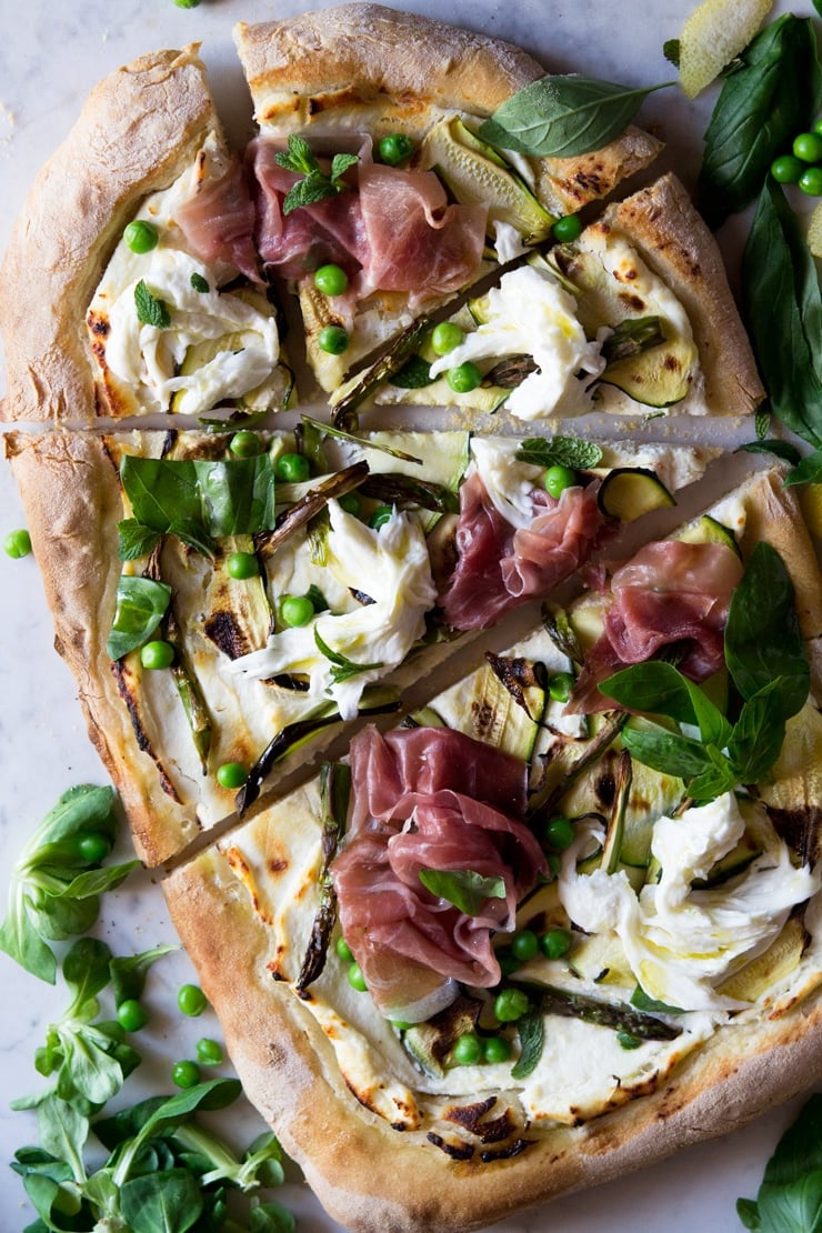 An overhead shot of a white base pizza with zucchini, prosciutto and asparagus