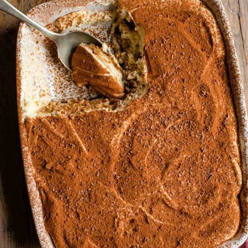 an overhead shot of a tiramisu in a dish with a slice out