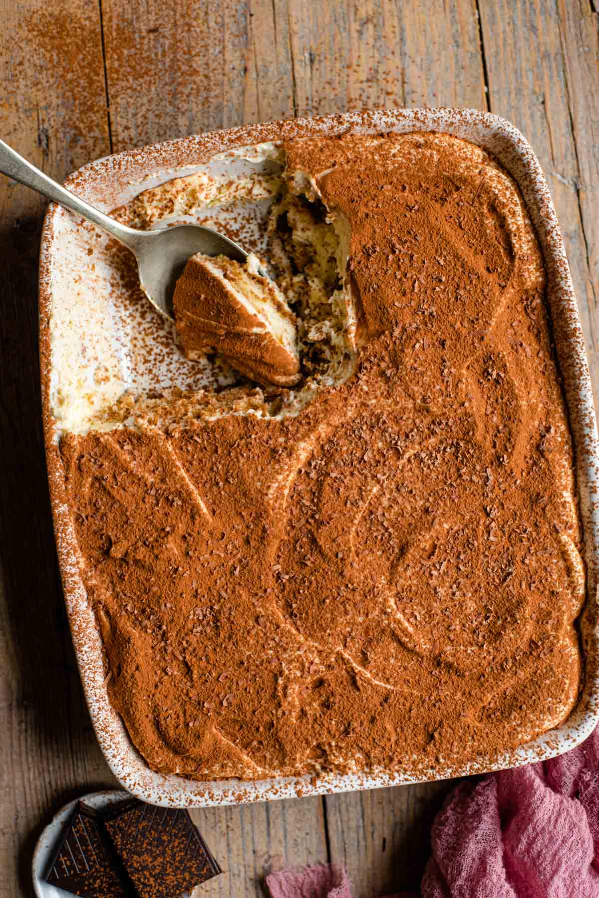 An overhead shot of a tiramisu in a dish with a slice out