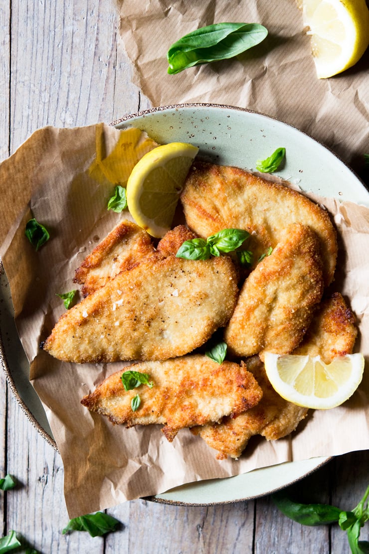 An overhead shot of breaded chicken cutlets on a plate garnished with basil