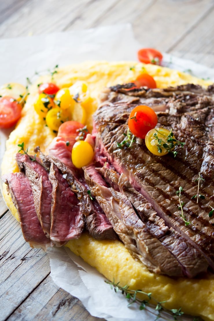 A side view of a florentine steak cut into slices (rare) topped with cherry tomatoes