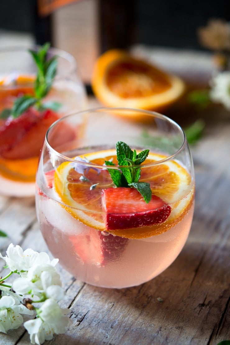 A close up of a glass filled with a cointreau rose cocktail garnished with mint and strawberries 