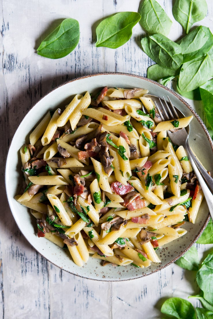 A photo of mushroom spinach pasta on a large plate with spinach scattered at the side