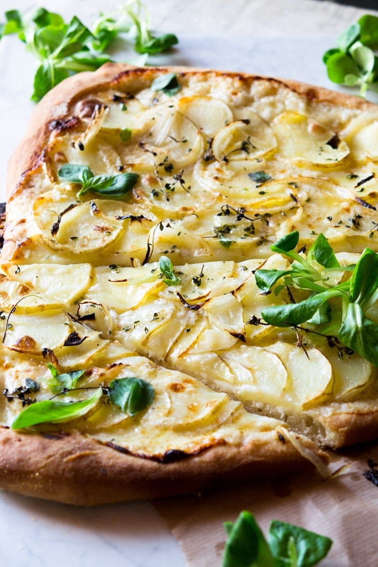 A side shot close up of a potato pizza on a marble work surface