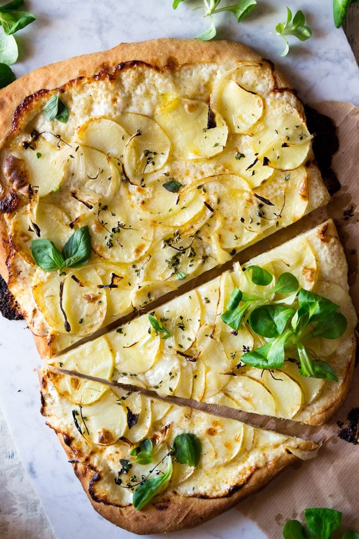 An overhead shot of a cheesy potato pizza with a large slice cut