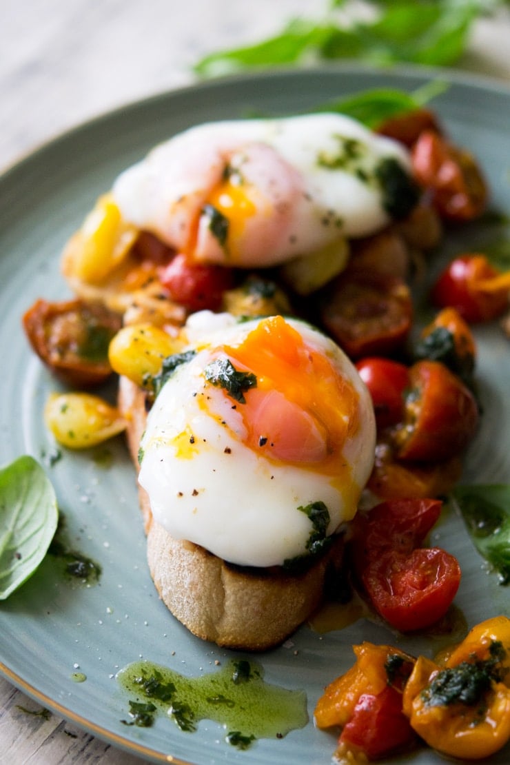 A close up of a oozing poached egg sitting on top of tomato breakfast crostini