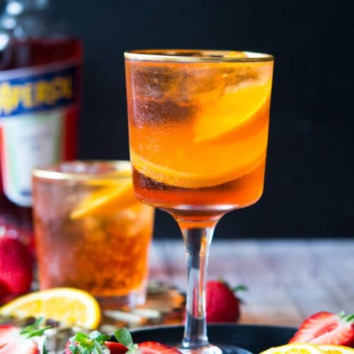 An aperol spritz cocktail in a wine glass with strawberries and oranges