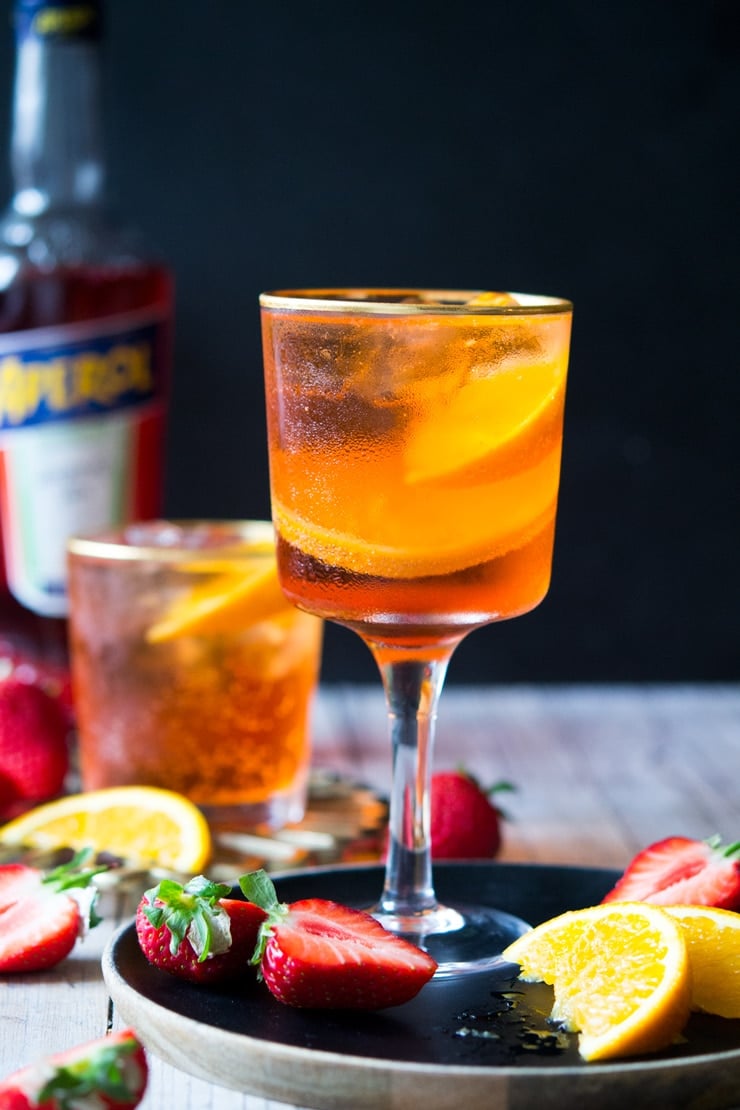 An aperol spritz cocktail in a wine glass with strawberries and oranges