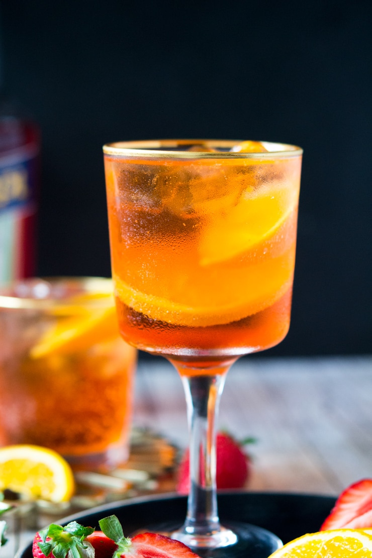 A close up of an Aperol spritz cocktail in a glass with strawberries and slices of orange at the side