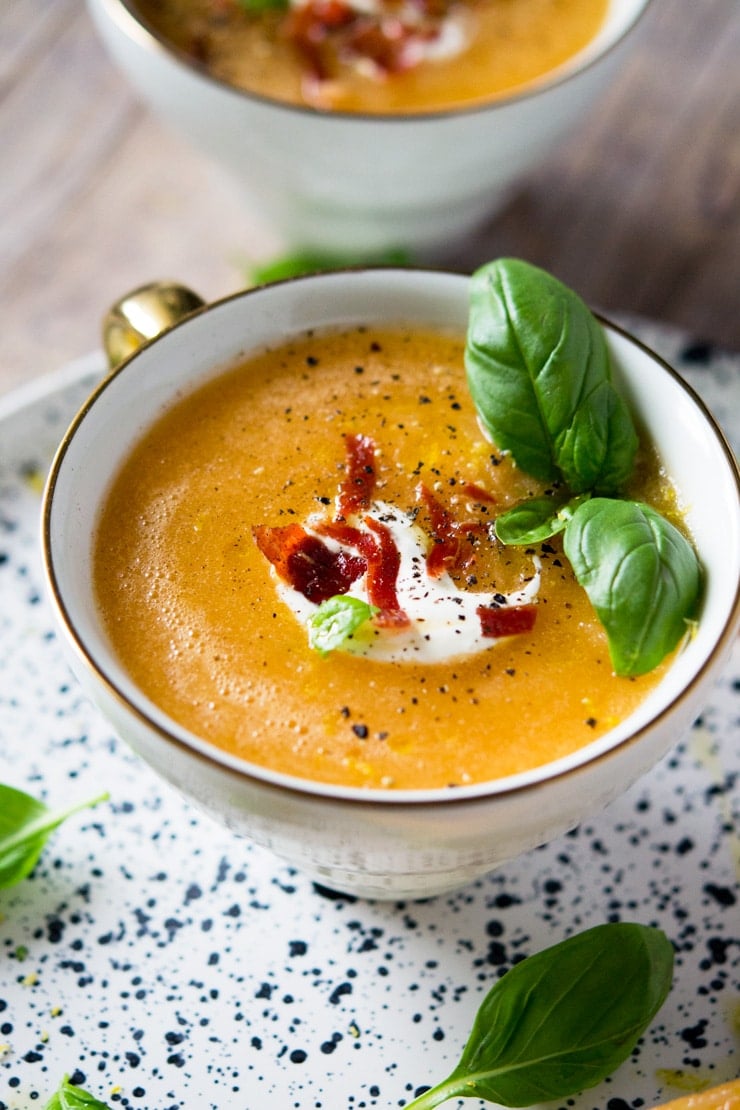 A close up of melon gazpacho soup in a mug topped with yogurt and prosciutto