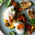 An overhead shot of sauted tomato breakfast crostini topped with poached eggs on a plate