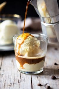 A photo of coffee getting poured over ice cream in a glass to make an affogato