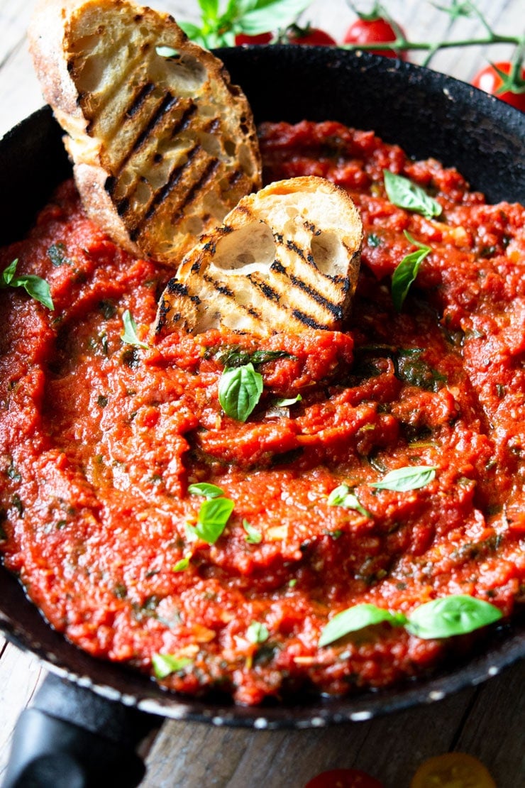 Italian tomato sauce in a sauce pan garnished with basil and two slices of ciabatta bread at the side