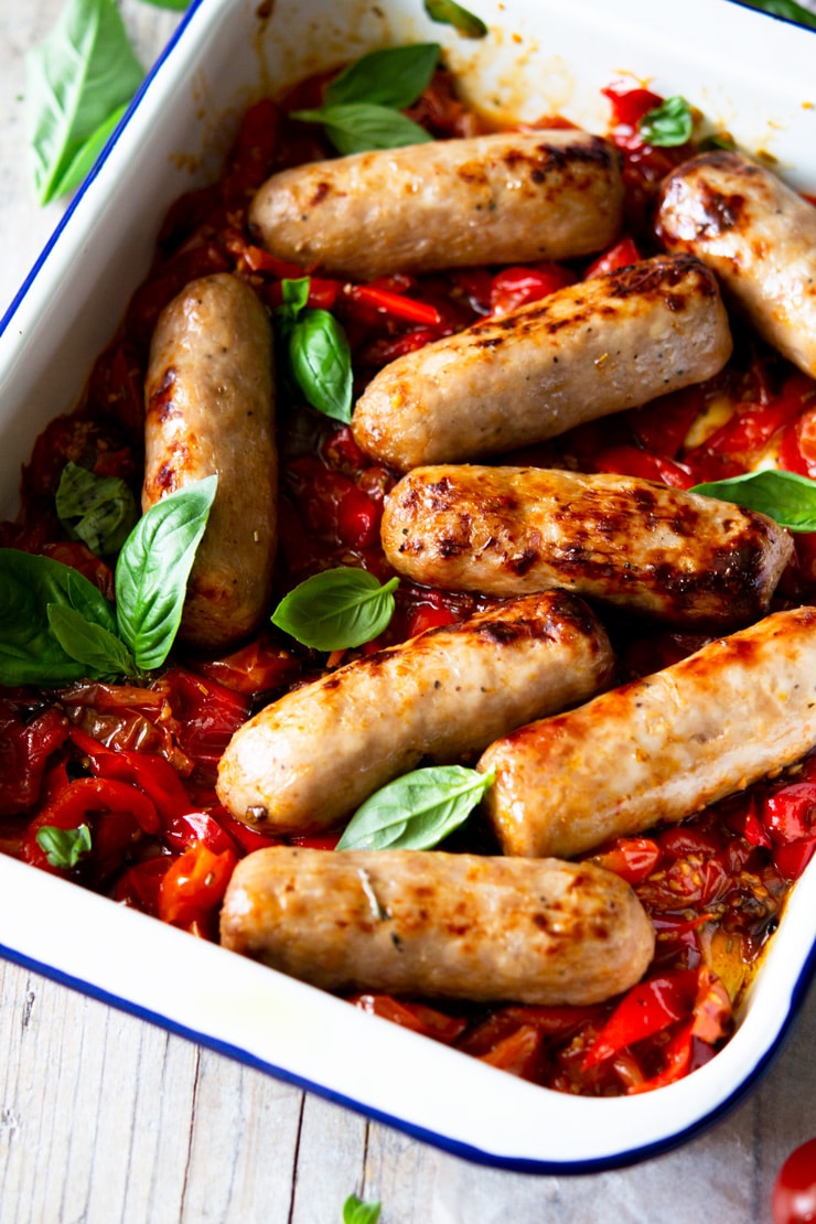 A close up of an Italian sausage bake with tomatoes and basil leaves