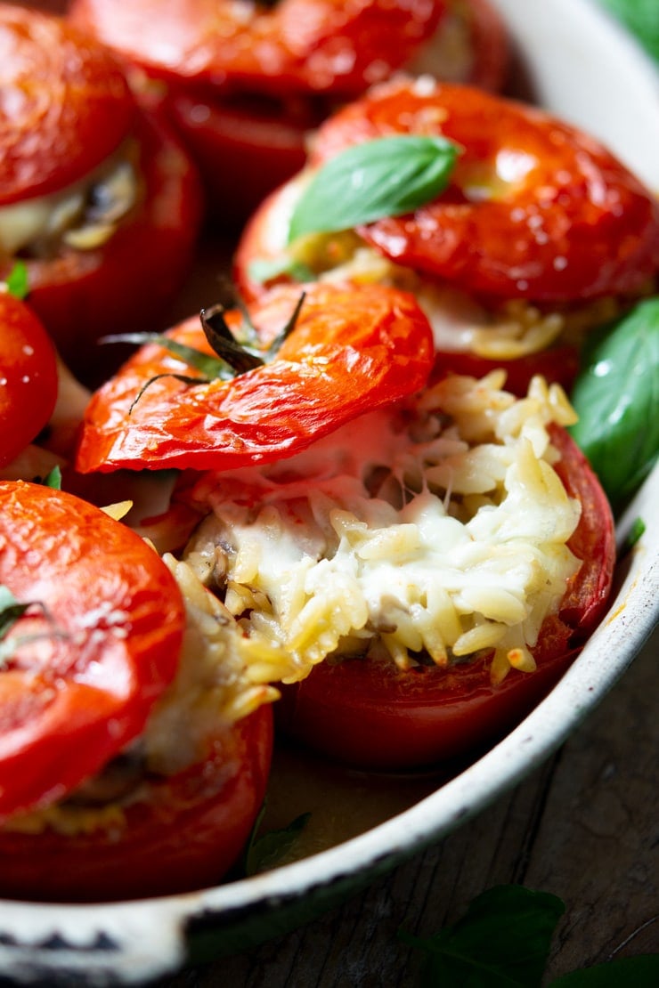 A close up of stuffed tomatoes in a baking dish filled with pasta and stretchy mozzarella cheese