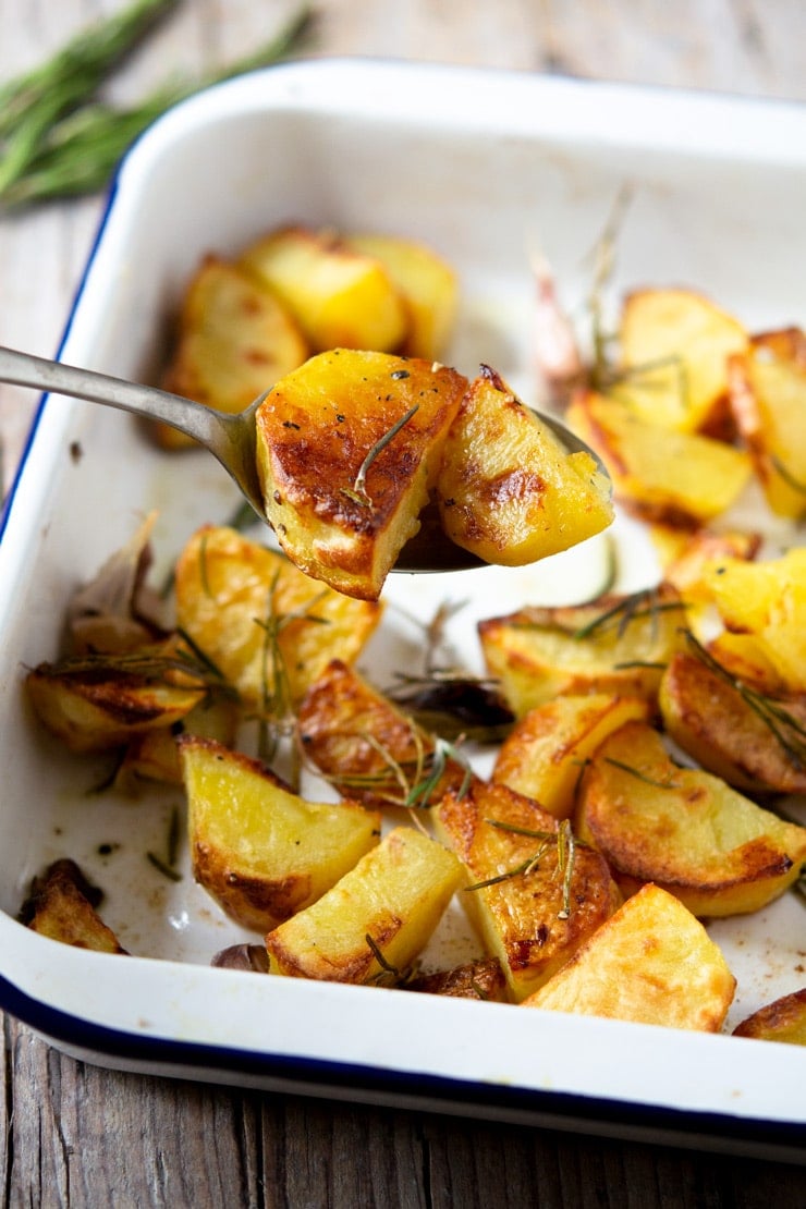 A spoon scooping up some Italian roast potatoes from a baking tray