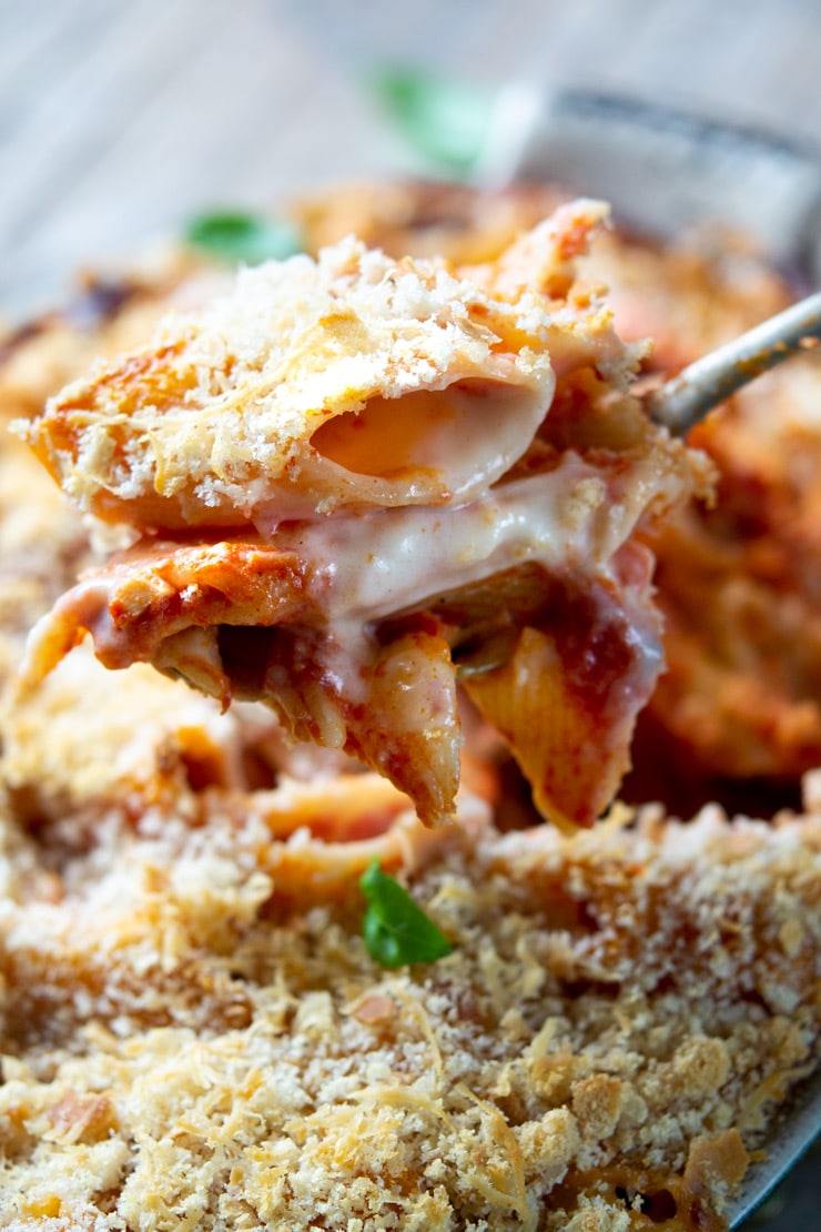 A close up of a spoon holding some oven baked pasta with cheese oozing