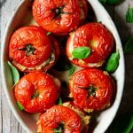 A square image of baked stuffed tomatoes in a baking dish
