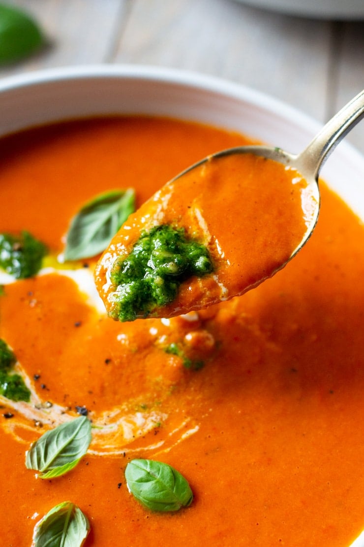 A spoon scooping up some roasted red pepper soup topped with pesto