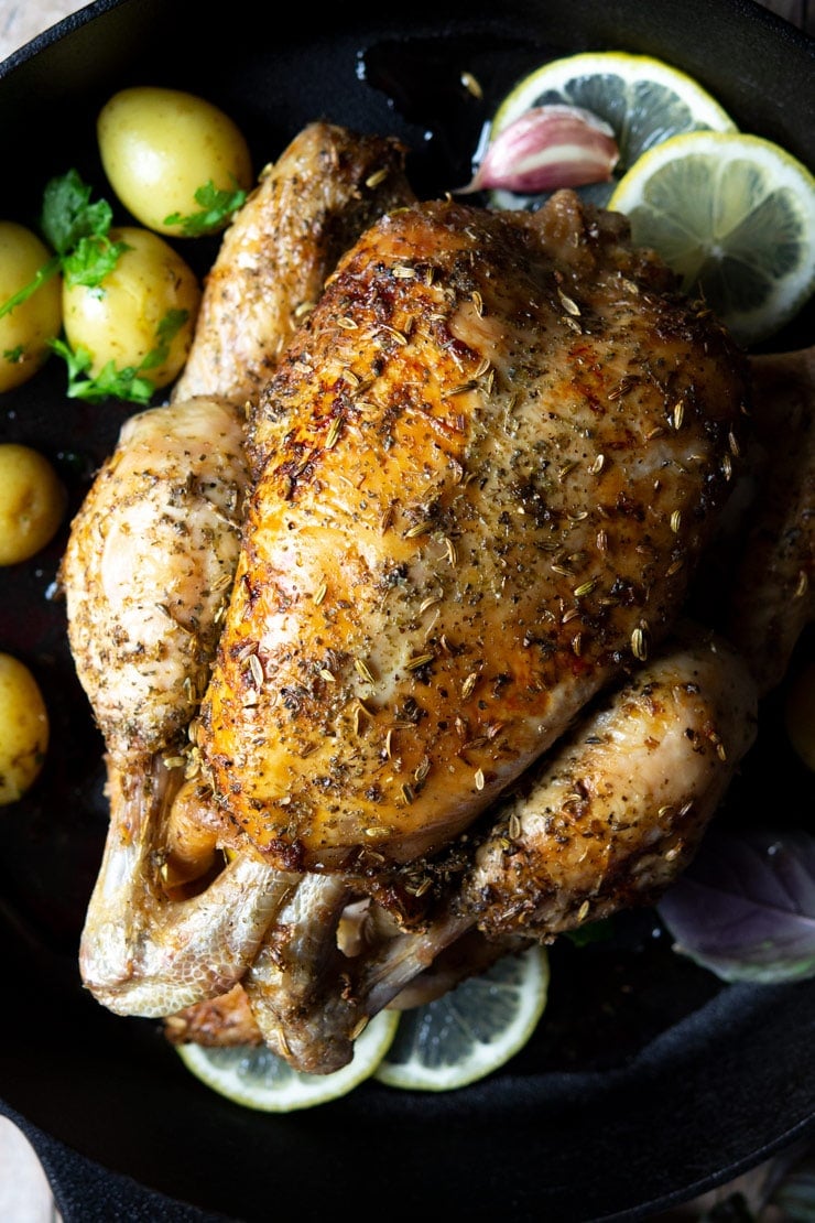 A close up of a lemon roast chicken in a cast iron skillet with potatoes and garlic