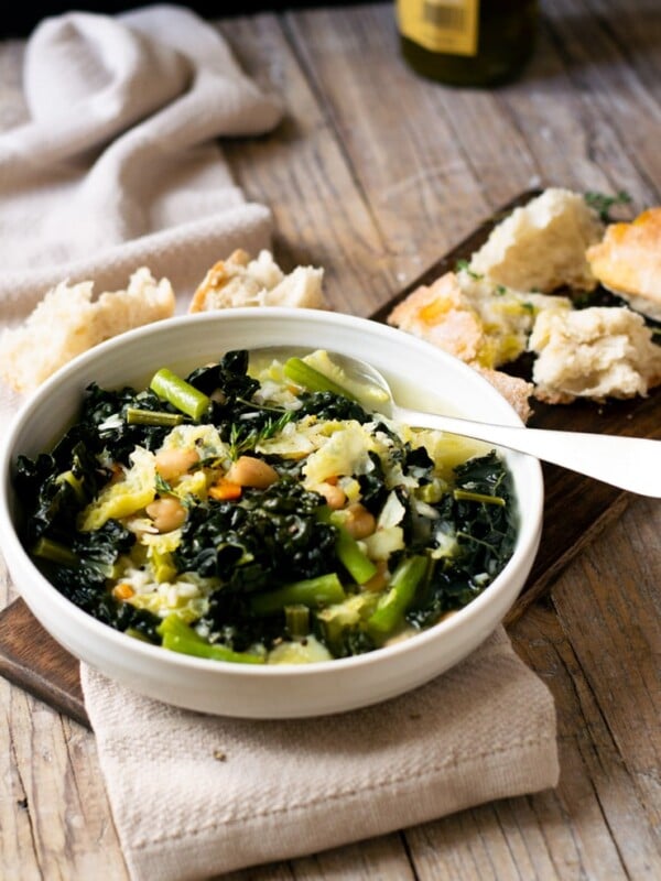 A bowl of Tuscan minestrone soup on a wooden surface with bread